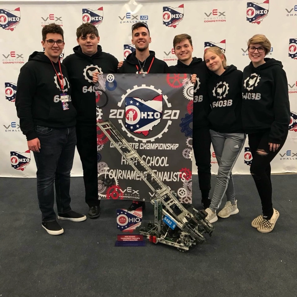 Team 6403B standing behind their robot with the middle person holding a states tournament finalists poster, 6 people left to right